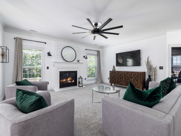 Modern living room with white walls, gray furniture, emerald green velvet pillows, wood console, and a central fireplace.